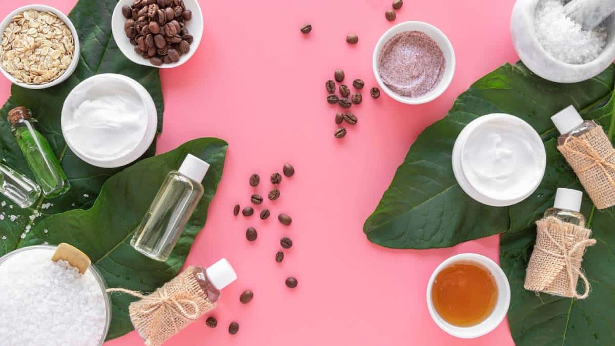 Top view of natural skincare products with leaves and ingredients on a pink background.