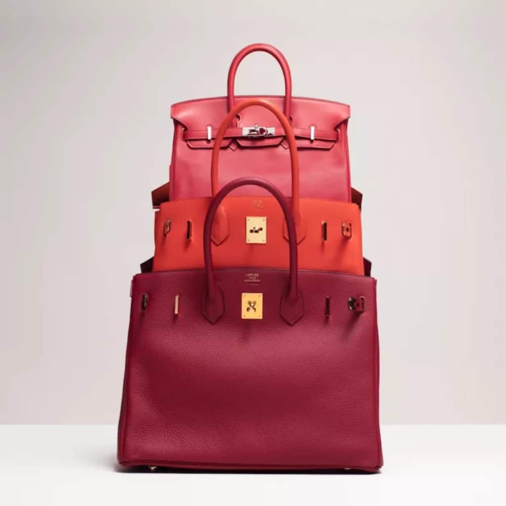 Stack of three luxurious red handbags of varying sizes on a light background.
