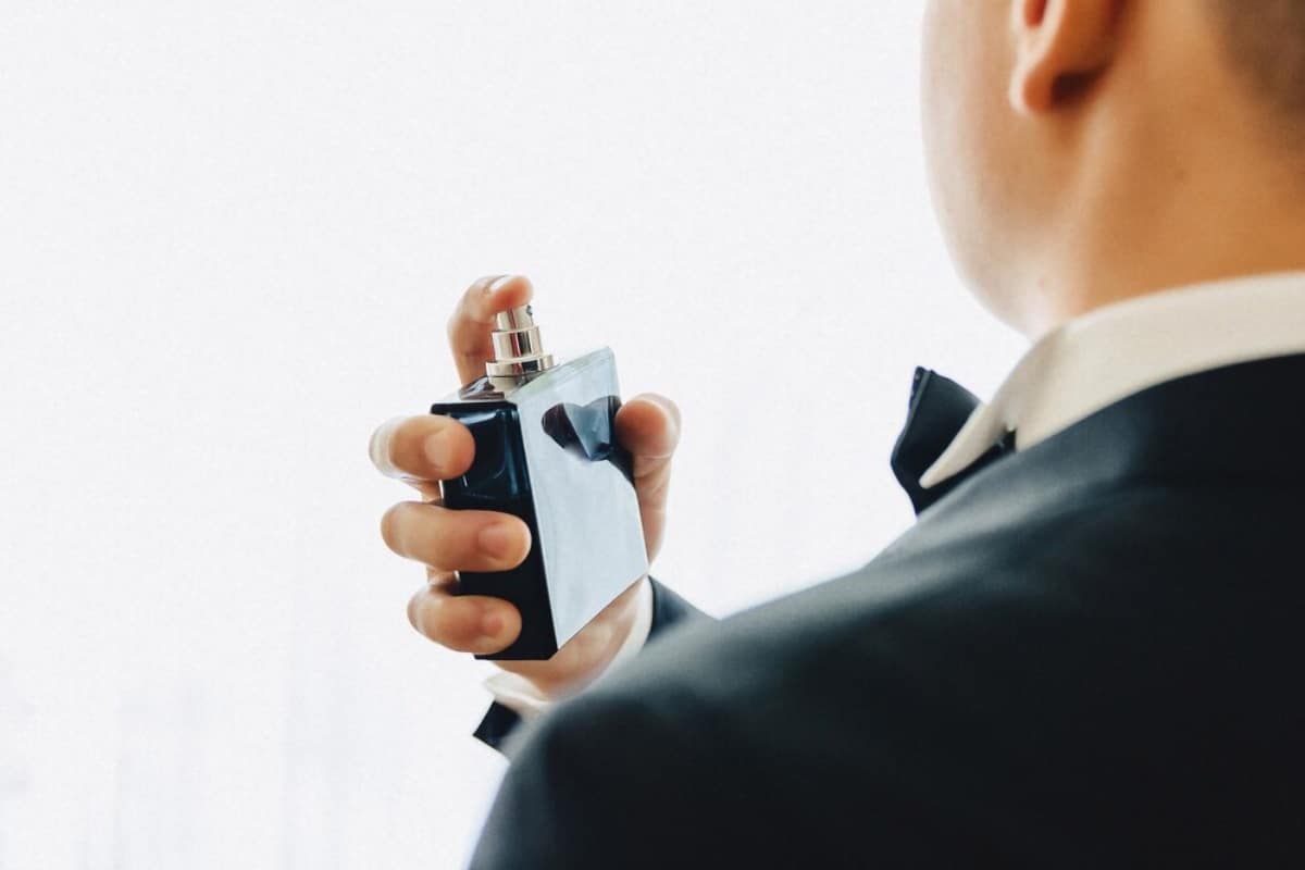 Man in suit using a cologne bottle, close-up of hand and bottle.