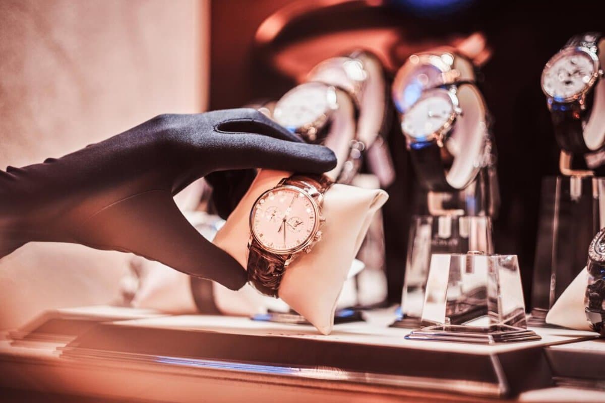 A gloved hand placing a luxury wristwatch on a display pillow among other watches.