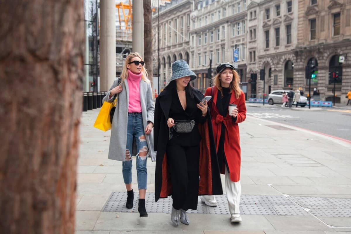 Three women walking on a city street, chatting and carrying shopping bags.