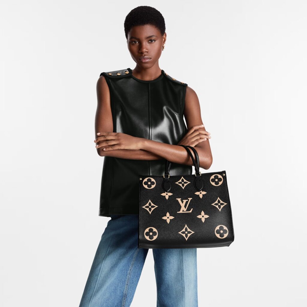 A woman in a black sleeveless top and jeans holding a designer handbag.