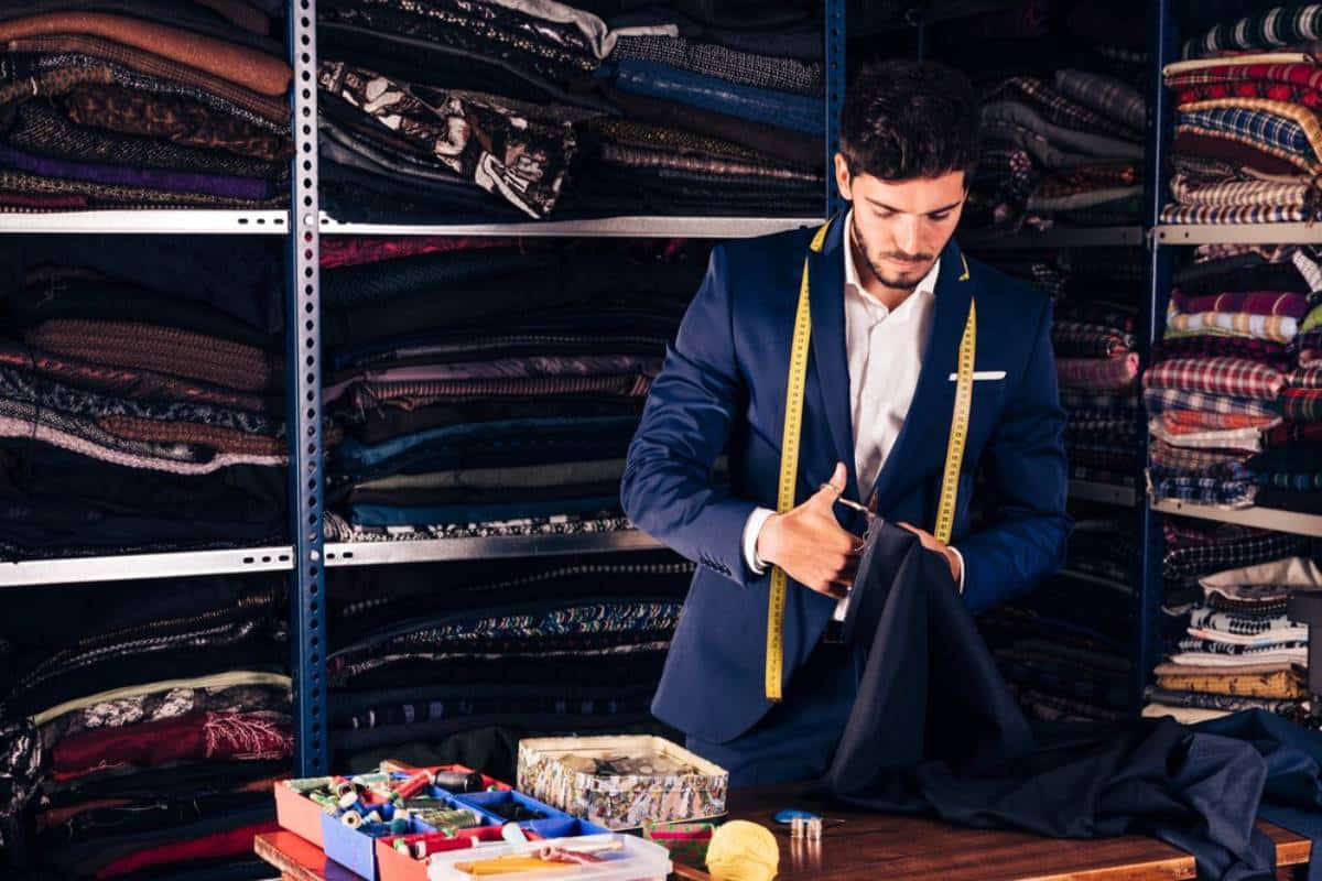 Tailor measuring fabric in a workshop filled with shelves of diverse textiles.