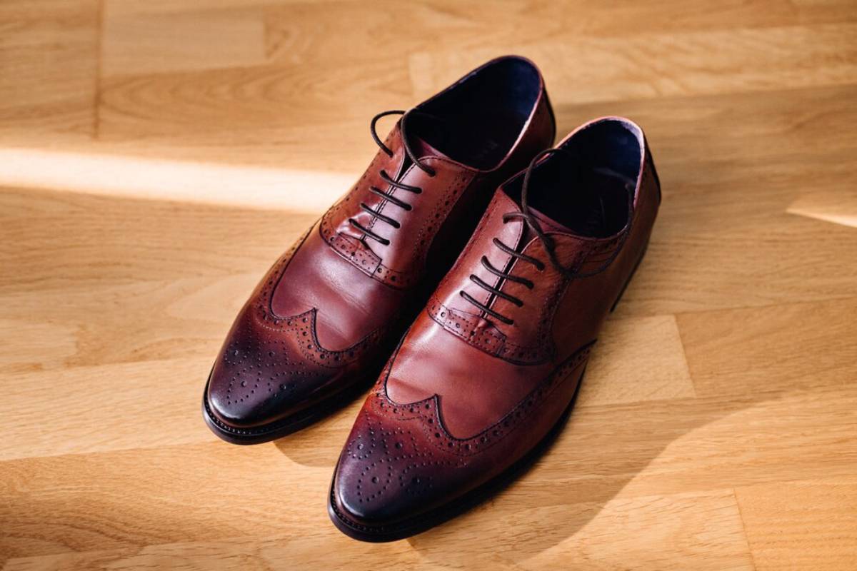 A pair of polished, burgundy brogue shoes on a wooden floor.